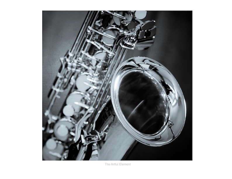 May include: A close-up, black and white photograph of a saxophone. The instrument's shiny, silver-colored body and keys are in sharp focus, with the bell prominently displayed. The image captures the details of the musical instrument.
