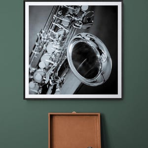 May include: Black and white framed photograph of a saxophone. The saxophone is silver and black, with intricate details. Below the photograph is a brown vintage record player with a black vinyl record.