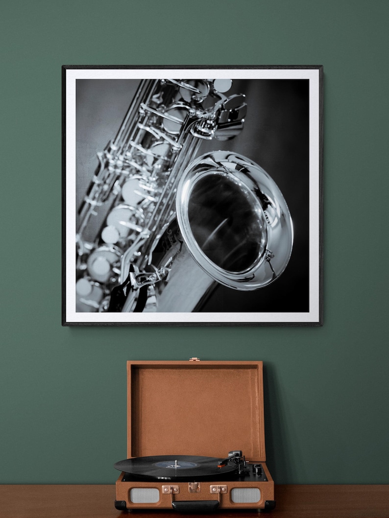 May include: Black and white framed photograph of a saxophone. The saxophone is silver and black, with intricate details. Below the photograph is a brown vintage record player with a black vinyl record.