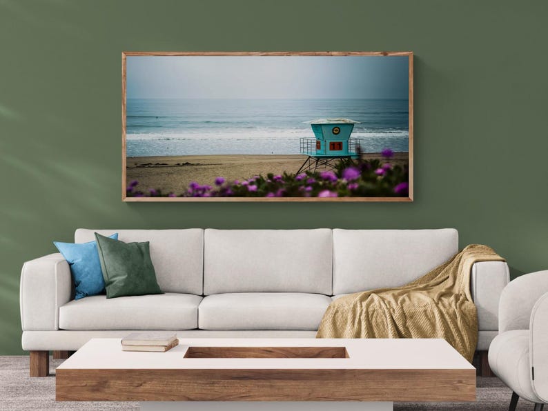 Panoramic color photograph of a california beach with lifeguard tower number 11 on an overcast morning. Out of focus purple flowers are in the foreground.