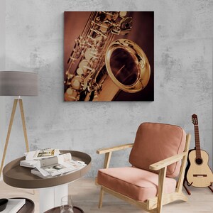 May include: A close-up of a saxophone print on canvas. The saxophone is gold-colored with intricate details, set against a dark background. The print is displayed on a gray wall, with a chair and guitar in the room.