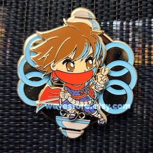May include: A gold-colored enamel pin featuring a cartoon ninja character with brown hair, a red scarf, and blue accents. The pin has a light blue and gold circular design around the character. The text "wavesstore.etsy.com" is visible.