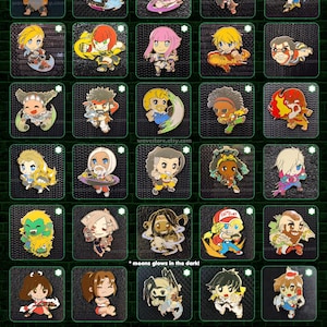 May include: A collection of Street Fighter 6 enamel pins, each 1.5"-2" in size, featuring various characters in a colorful, cartoon style. The pins are set against a dark green background, with some pins that glow in the dark.