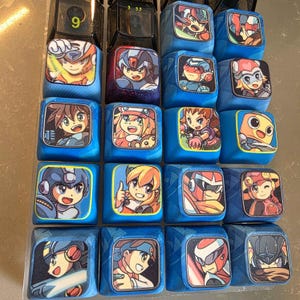 May include: A collection of twenty square mechanical keyboard keycaps arranged in a grid. Each keycap features a unique, colorful anime-style character illustration printed on the top surface, with blue, black, and purple base colors.