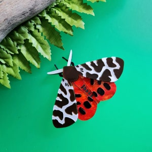 Może przedstawiać: Czarno-biały motyl z czerwonymi i pomarańczowymi skrzydłami. Motyl jest wykonany z akrylu i ma efekt 3D.
