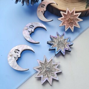 May include: Five decorative ornaments, two crescent moons and three stars, with iridescent finishes and pearl accents. The ornaments are made of wood and have a whimsical, celestial theme.