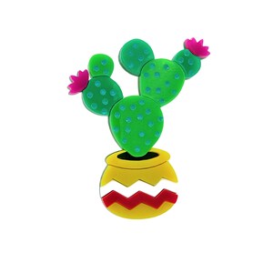 Puede incluir: Un cactus verde con flores rosas en una maceta amarilla con un patrón de zigzag rojo y blanco.