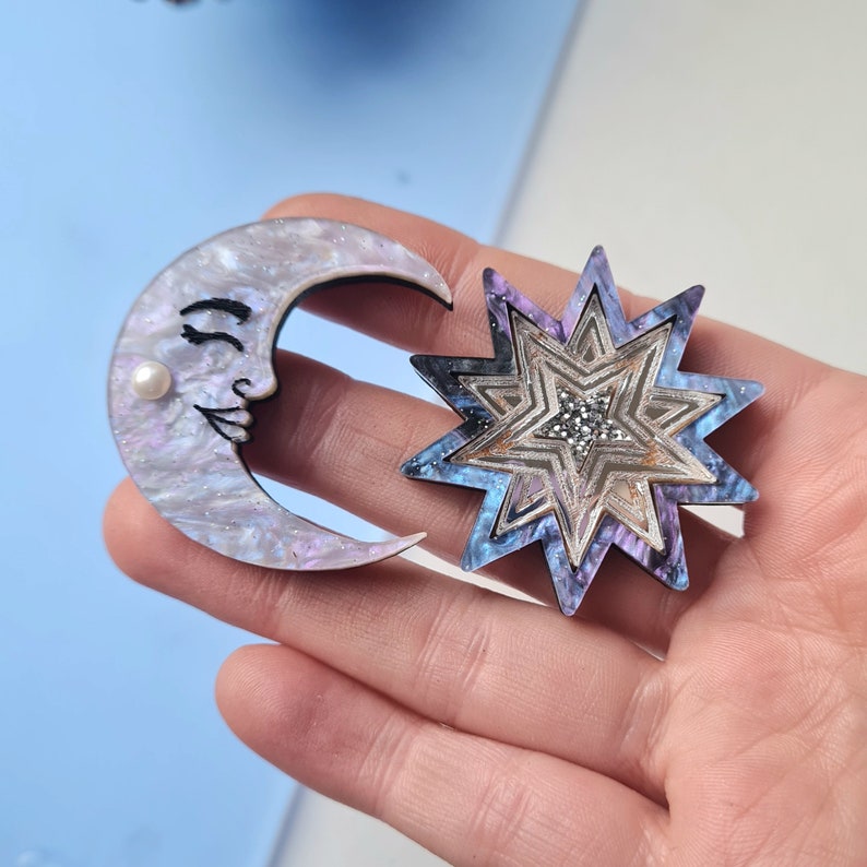 May include: A set of two decorative wooden ornaments, a crescent moon with a face and a multi-layered star with a galaxy design.