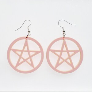 May include: A pair of pink earrings with a pentagram design. The earrings are made of acrylic and have silver hooks.