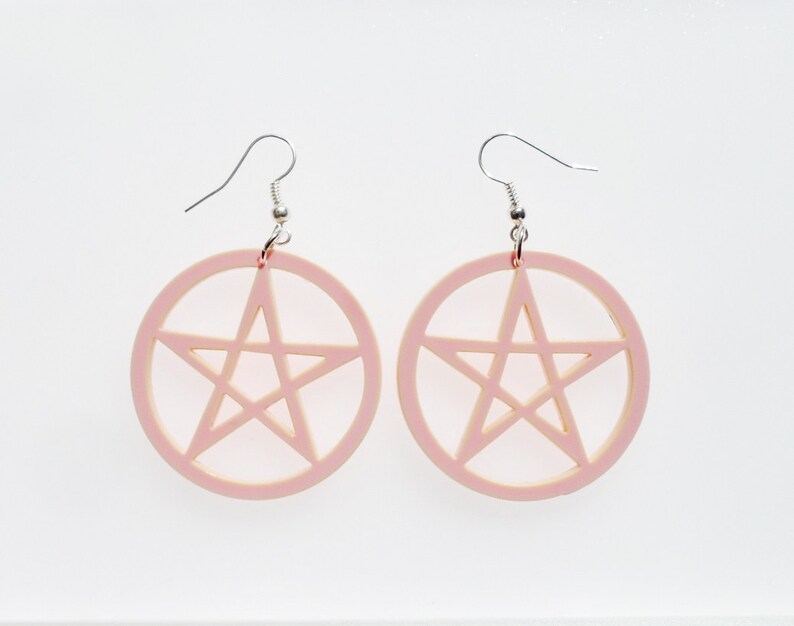 May include: A pair of pink earrings with a pentagram design. The earrings are made of acrylic and have silver hooks.