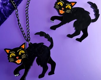 May include: A black necklace with two black cat charms. The cats have orange eyes and are in a playful pose.