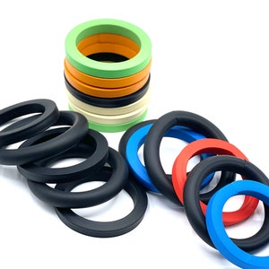 May include: Assortment of colorful rubber O-rings in various sizes. The rings are stacked in a pile and laid out on a white surface.