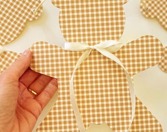 Può includere: Una ghirlanda decorativa con molteplici sagome a forma di orso con un motivo a quadretti vichy marrone e crema. Ogni orso ha un nastro di raso bianco legato a fiocco attorno al collo ed è infilato su un filo sottile. Il testo recita Brown & Cream Gingham.