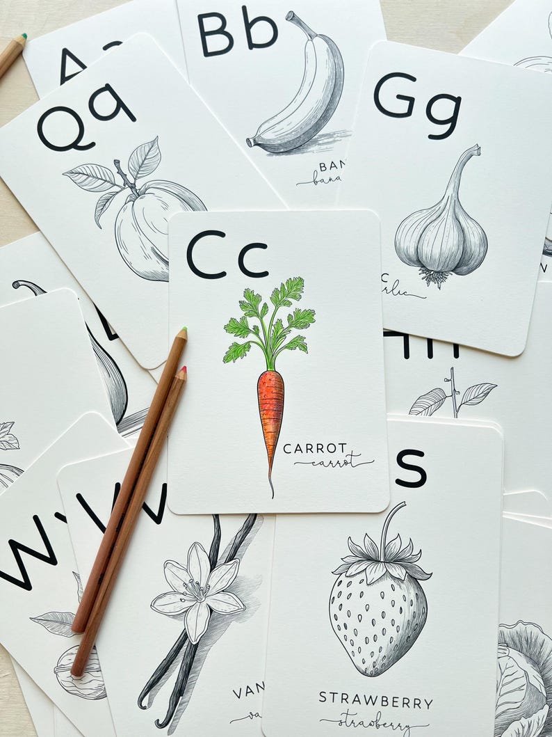 May include: A collection of white flashcards with black and white illustrations of fruits and vegetables, including a carrot, banana, and strawberry. The letter 'C' is above the carrot illustration. Two pencils are on the left side.