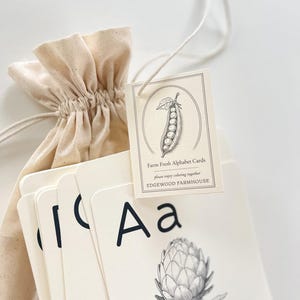May include: A set of Farm Fresh Alphabet Cards with a drawstring bag. The cards feature black uppercase and lowercase letters, and botanical illustrations. The tag reads "Farm Fresh Alphabet Cards" and "Edgewood Farmhouse".
