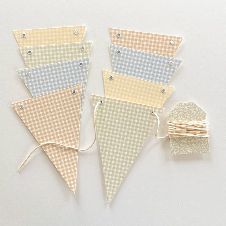 May include: A set of pastel-colored gingham pattern pennant flags. The flags are in shades of yellow, blue, beige, and green. A tag with a floral pattern and string is included. The flags are connected with a white string.
