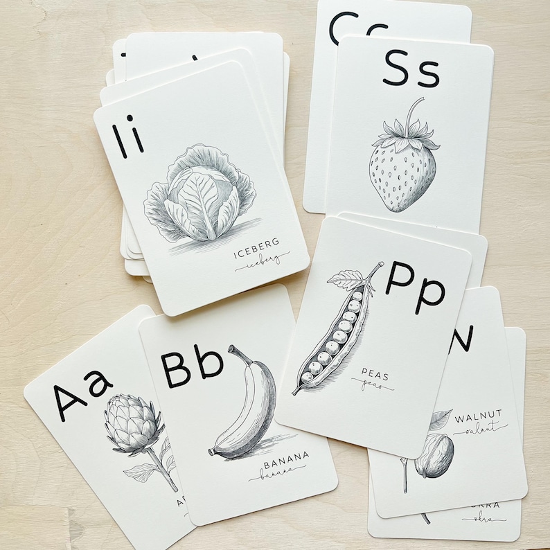 May include: A collection of white flashcards featuring black illustrations of fruits and vegetables. Each card displays a letter of the alphabet and the name of the item. The cards include a cabbage, strawberry, banana, and peas.