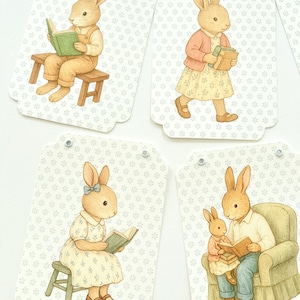 May include: Set of four gift tags featuring illustrations of rabbits. Each tag has a different scene: a rabbit reading, carrying books, sitting on a stool reading, and a parent rabbit reading to a child. The tags have a floral pattern background.