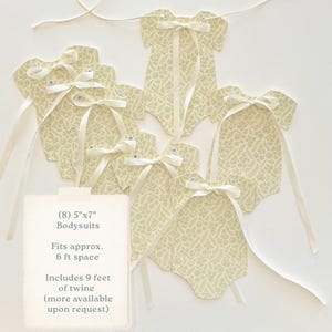 May include: A garland of eight paper bodysuits, each measuring 5" x 7", with a cream-colored fern pattern. Each bodysuit has a cream ribbon bow and is strung on twine. The garland is suitable for a 6 ft space.