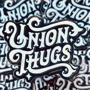 May include: A close-up of a stack of black and white stickers with the text "Union Thugs" in a stylized font. The stickers are printed with a white background and black lettering. The text "Lynn Grove" is printed in smaller letters below the main text.