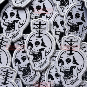 May include: A close-up of several white embroidered patches featuring a black and white skull with a power line running through it. The text "LYNNGROVE" is embroidered on each patch.