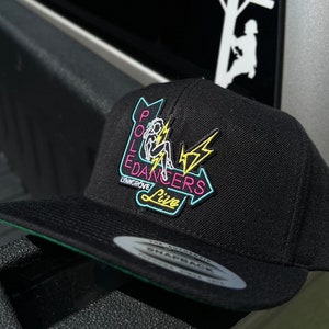 May include: Black and green baseball cap with a neon pink, yellow, and blue patch that says "Pole Dancers Live" with a silhouette of a woman climbing a pole. The patch also says "Lynn Grove" in a smaller font.