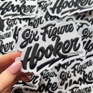 May include: Close-up of several white fabric patches with black embroidered text that reads "Six Figure Hooker" with the company name "LYNNGROVE" printed below the text.