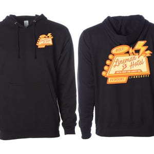 May include: Black hooded sweatshirt with a front pocket and drawstring. The front features a small orange and yellow graphic. The back displays a larger graphic with the words "Lineman Hotel" and "24 Hours" in orange and yellow.