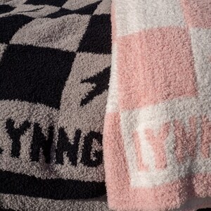 K&ouml;nnte beinhalten: Zwei Pl&uuml;schdecken mit karierten Mustern. Eine Decke ist schwarz und grau mit dem Wort "YING" in schwarzen Buchstaben. Die andere Decke ist rosa und wei&szlig; mit dem Wort "LIVING" in wei&szlig;en Buchstaben.