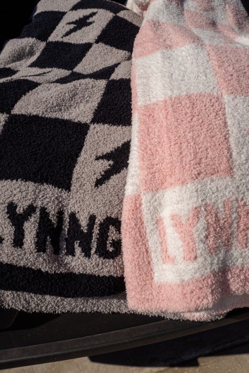 K&ouml;nnte beinhalten: Zwei Pl&uuml;schdecken mit karierten Mustern. Eine Decke ist schwarz und grau mit dem Wort "YING" in schwarzen Buchstaben. Die andere Decke ist rosa und wei&szlig; mit dem Wort "LIVING" in wei&szlig;en Buchstaben.