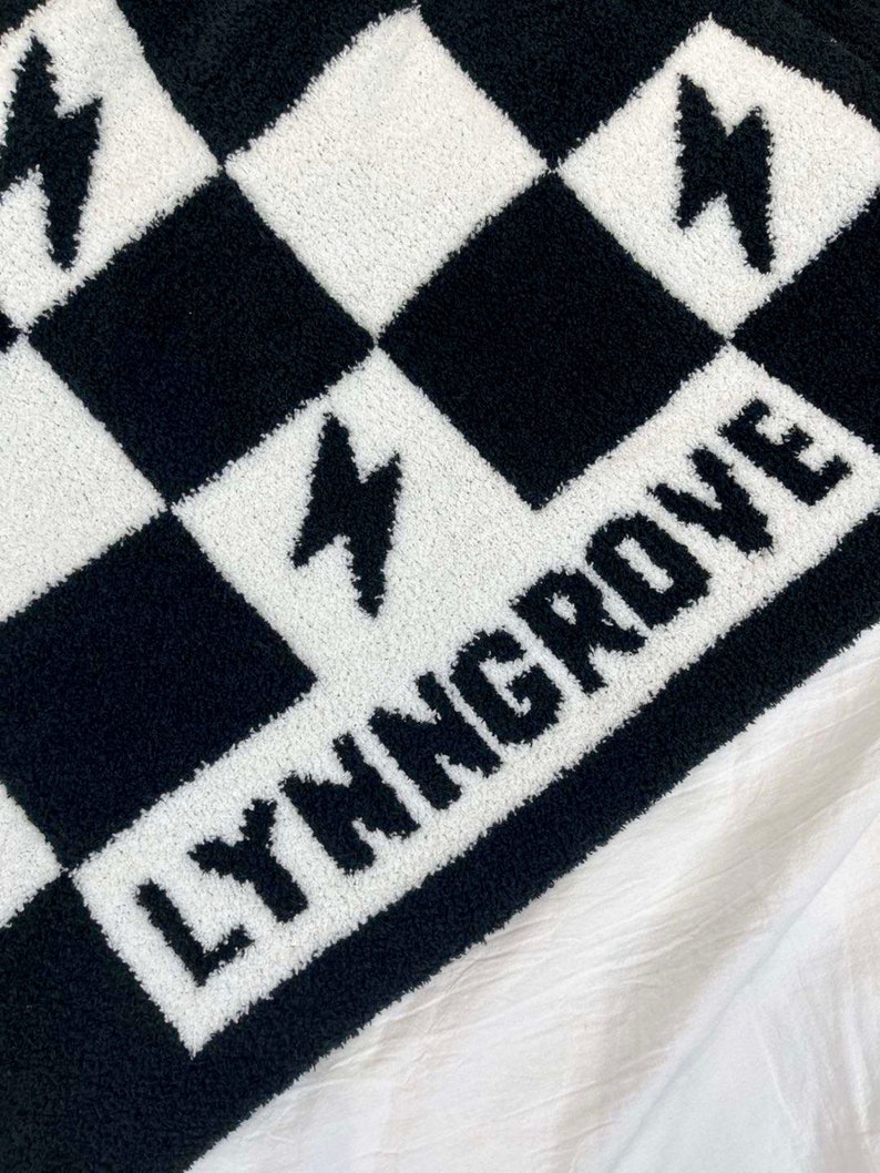 K&ouml;nnte beinhalten: Schwarze und wei&szlig;e karierte Fleece-Decke mit dem Wort "LYMNGROVE" in wei&szlig;en Buchstaben.