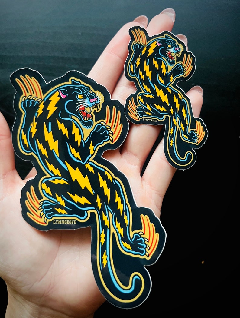 May include: Two black panther stickers with yellow lightning bolt patterns. The larger sticker is 5 inches tall and the smaller sticker is 3 inches tall. Both stickers have the text "LYNNGROVE" printed on them.