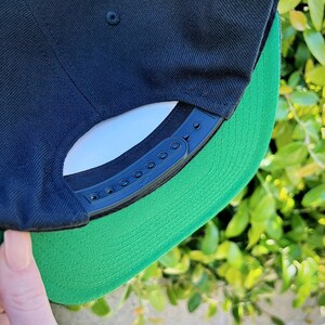 May include: A black and green baseball cap with a black plastic strap and adjustable buckle. The cap has a green underside.