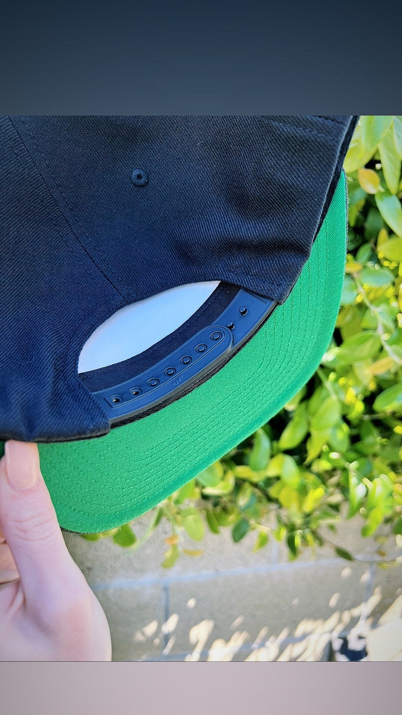 May include: A black and green baseball cap with a black plastic strap and adjustable buckle. The cap has a green underside.