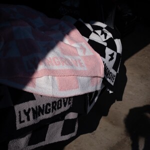 K&ouml;nnte beinhalten: Ein Stapel rosa, wei&szlig; und schwarz karierter Decken mit dem aufgedruckten Text "LYNNGROVE".