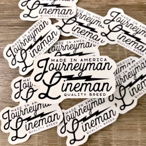 May include: A collection of white stickers with black text and a lightning bolt graphic. The text on the stickers reads "Made in America Journeyman Lineman Quality Breed".