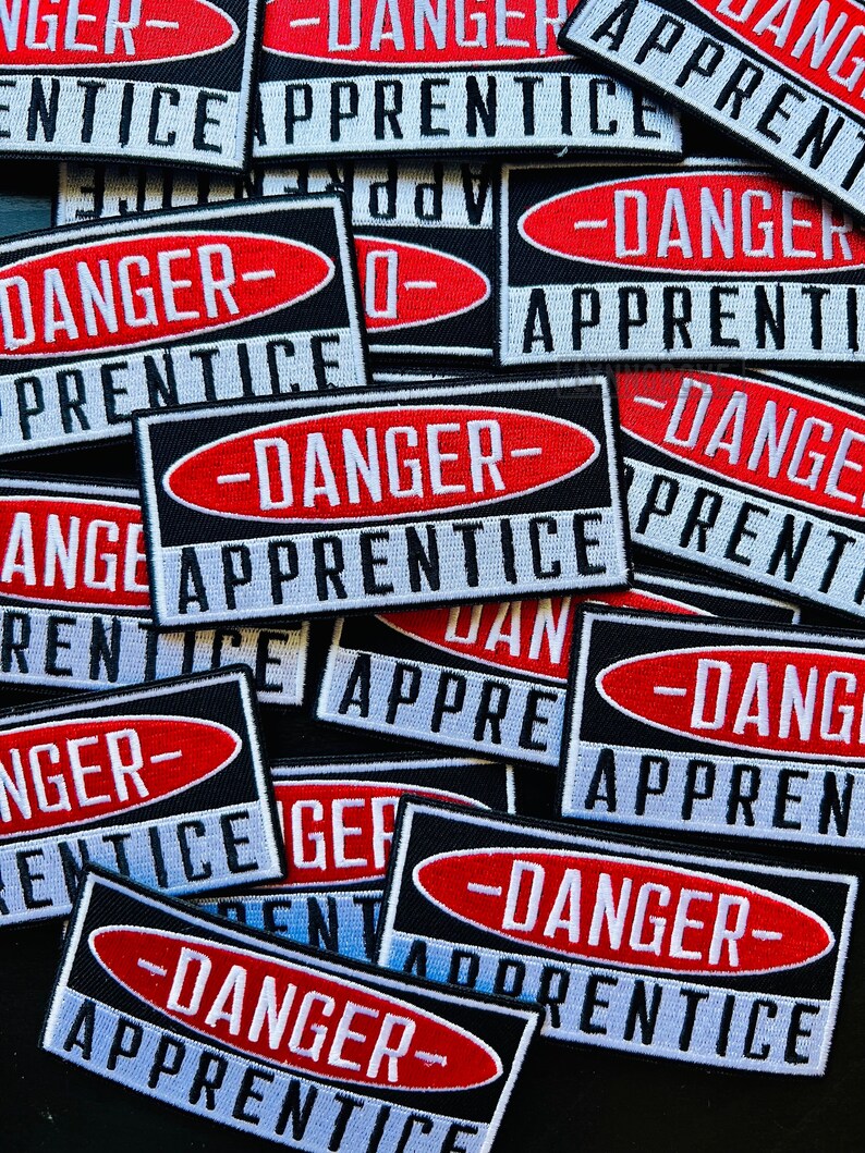 Puede incluir: Un mont&oacute;n de parches de tela negros y blancos con texto rojo y blanco que dice "Peligro - Aprendiz".