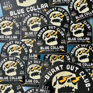 May include: A collection of black and yellow stickers with a skull graphic and the text "Burnt Out Club - Blue Collar - Members Only - Est. MMXXI - USA Made".