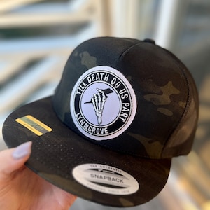May include: Black and green camouflage trucker hat with a white patch that says "Till Death Do Us Part" with a skeleton hand holding a lightning bolt. The patch also says "Lyngrove" at the bottom.