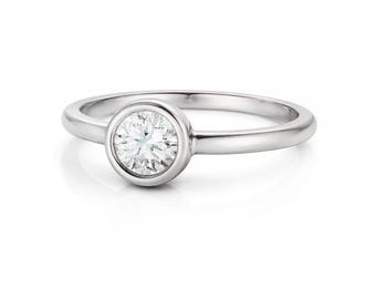 Puede incluir: Un anillo de plata con un diamante redondo y transparente engastado en bisel. La banda pulida complementa el diamante brillante. Este anillo, con su diseño clásico, es adecuado para compromisos o uso diario.