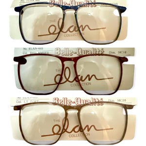 May include: Three pairs of vintage eyeglasses with brown, red, and blue frames. The frames are rectangular and have a classic style. The lenses are clear. The eyeglasses are labeled "The Elan Collection" and "Belle-Qualité".