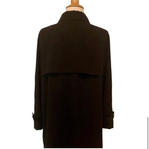 May include: A long, black trench coat with a collar and a single button closure. The coat has a simple design and is made of a smooth fabric.