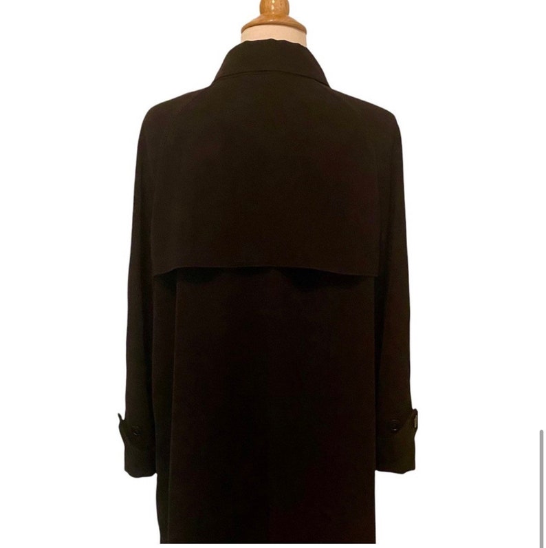 May include: A long, black trench coat with a collar and a single button closure. The coat has a simple design and is made of a smooth fabric.