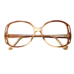 May include: A pair of large, round, brown-tinted eyeglasses with a thin, brown frame. The frame has a subtle, textured design. The lenses are clear.