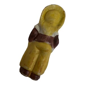 Puede incluir: Una peque&ntilde;a figurita de cer&aacute;mica de una persona vestida con un atuendo amarillo con detalles marrones. La figurita tiene un sombrero blanco y un cintur&oacute;n marr&oacute;n.