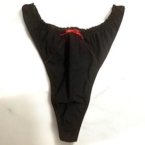 May include: Black thong underwear with a red bow at the front. The edges are trimmed with a darker fabric and the seams are stitched with red thread. The garment is made of a soft, opaque material.
