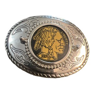 May include: Silver belt buckle featuring a black and gold design of a 1926 Buffalo nickel. The buckle has a decorative border with floral accents.
