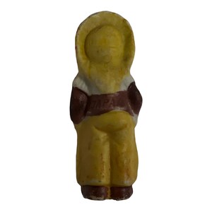 Puede incluir: Una figurita de cer&aacute;mica amarilla de una persona que lleva una chaqueta y pantalones marrones y blancos. La figurita tiene un cintur&oacute;n marr&oacute;n con la palabra "TAPA" escrita en &eacute;l.