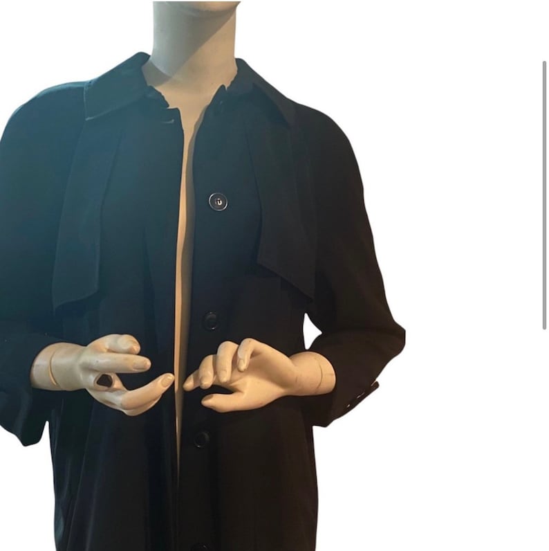 May include: A long black coat with a button-up front and a collar. The coat has a relaxed fit and is made of a smooth fabric.