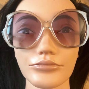 May include: White oversized sunglasses with a rounded, butterfly-shaped frame and tinted lenses.